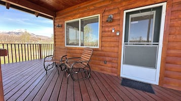 A wooden deck with two rocking chairs and a window with a mesh screen.