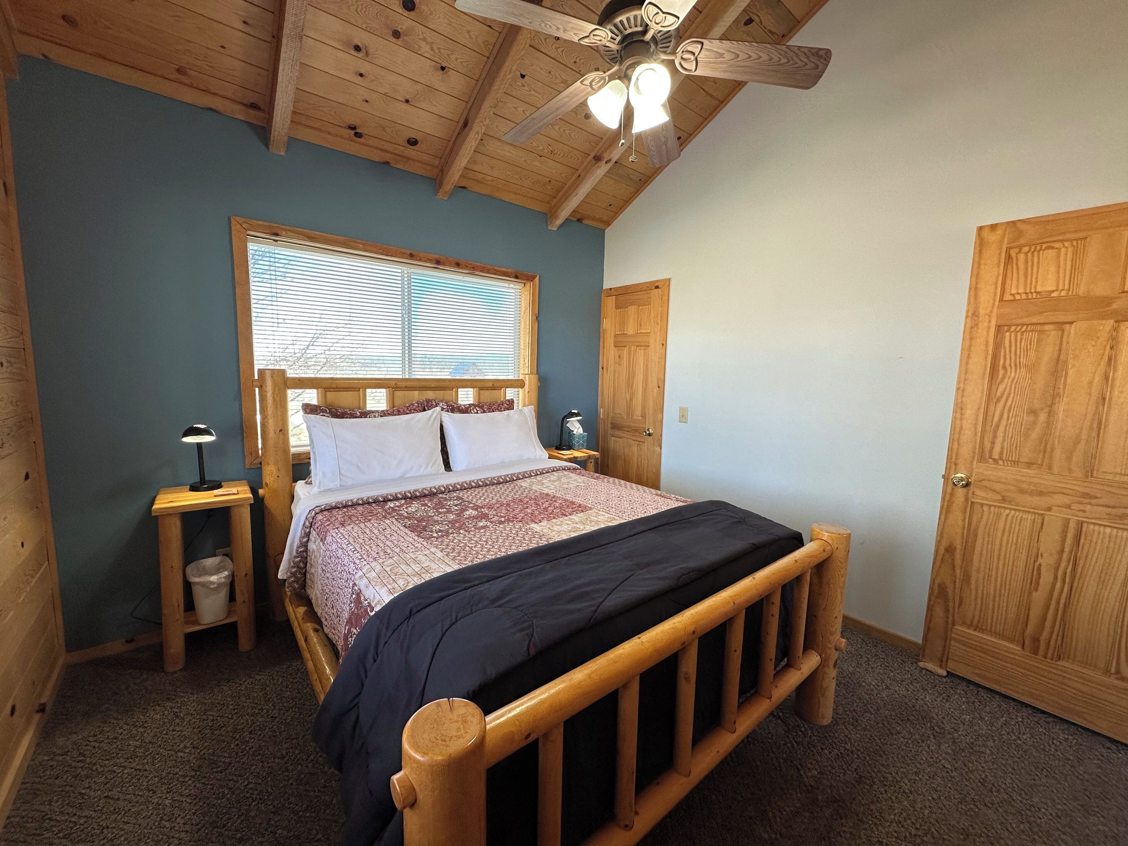 A bedroom with a wooden bed, a ceiling fan, a window with blinds, and a door.