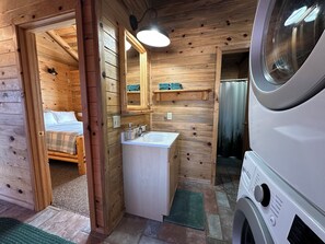 A wooden cabin interior with a bed, a sink, a mirror, and a washing machine. - Mount Peale Country Inn near Moab (La Sal)