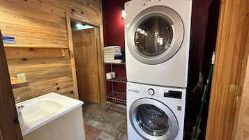 A laundry area with two stacked washing machines, a wooden wall, a door, and a sink.