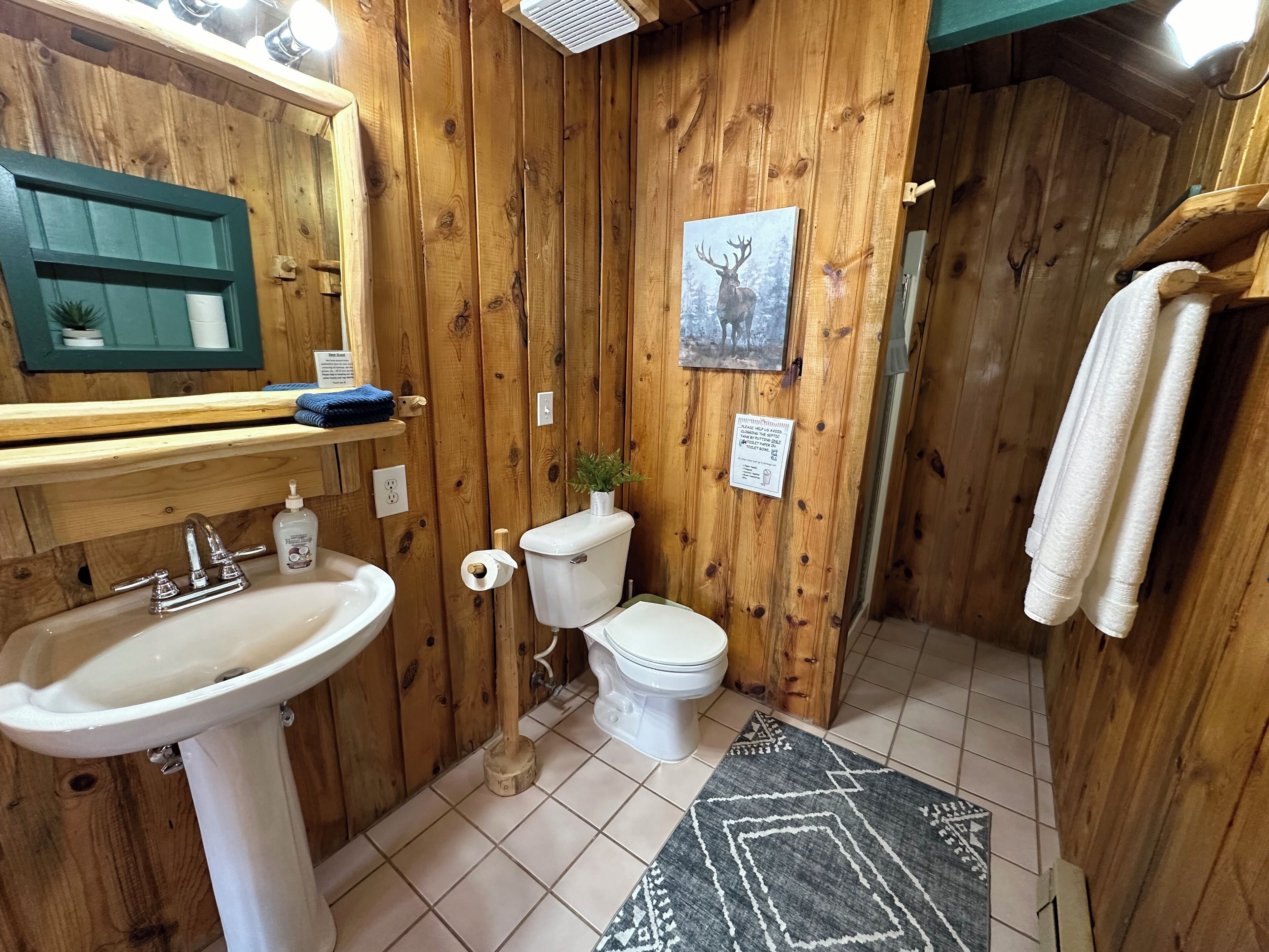 Een houten badkamer met een wastafel, toilet en een foto van een hert in een lijst aan de muur.