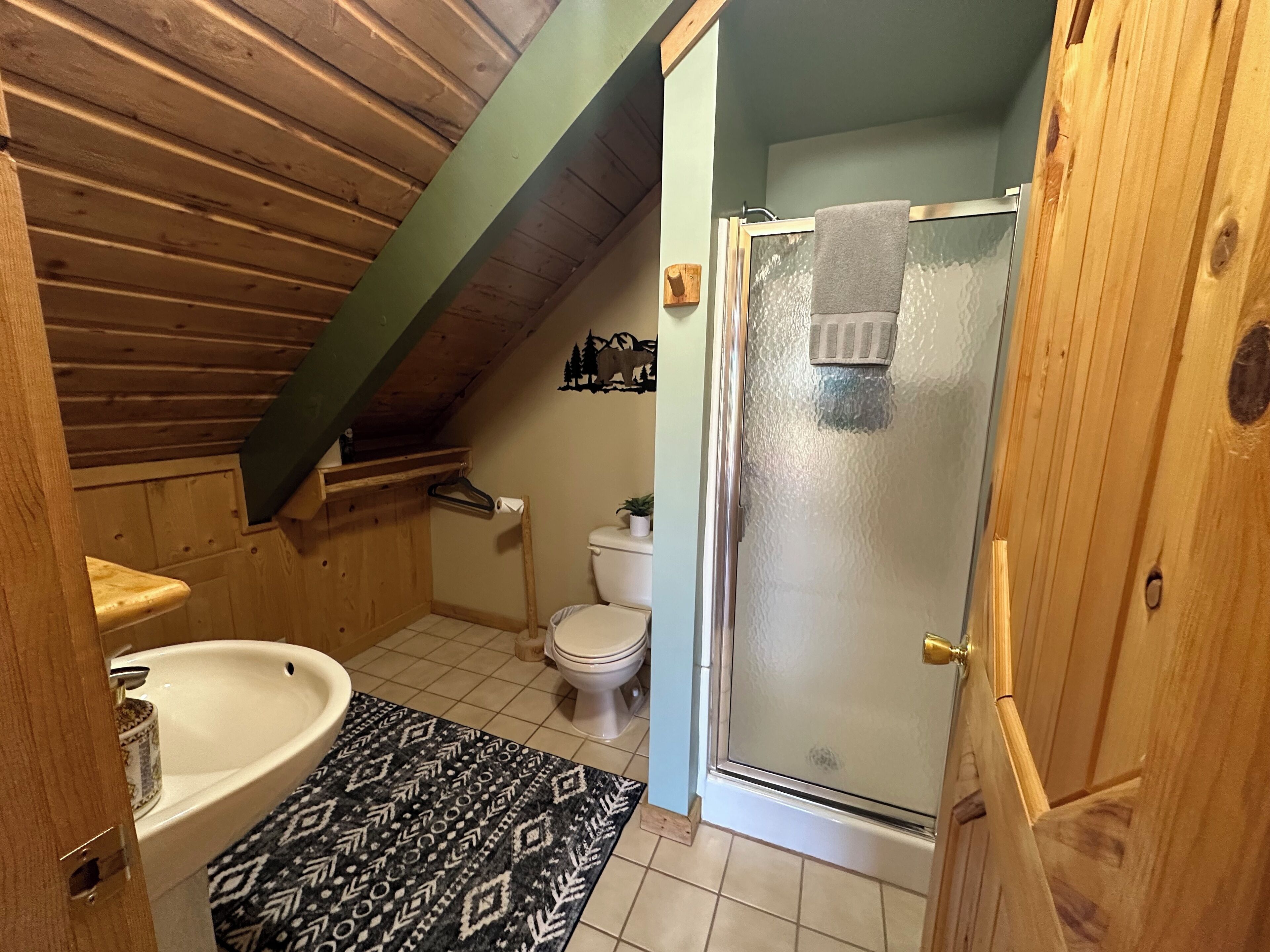 Un baño con techo de madera, una bañera, un inodoro y una puerta de ducha de cristal.