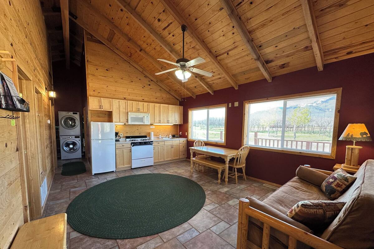 A wooden cabin interior with a kitchen, dining area, and a cozy seating area.