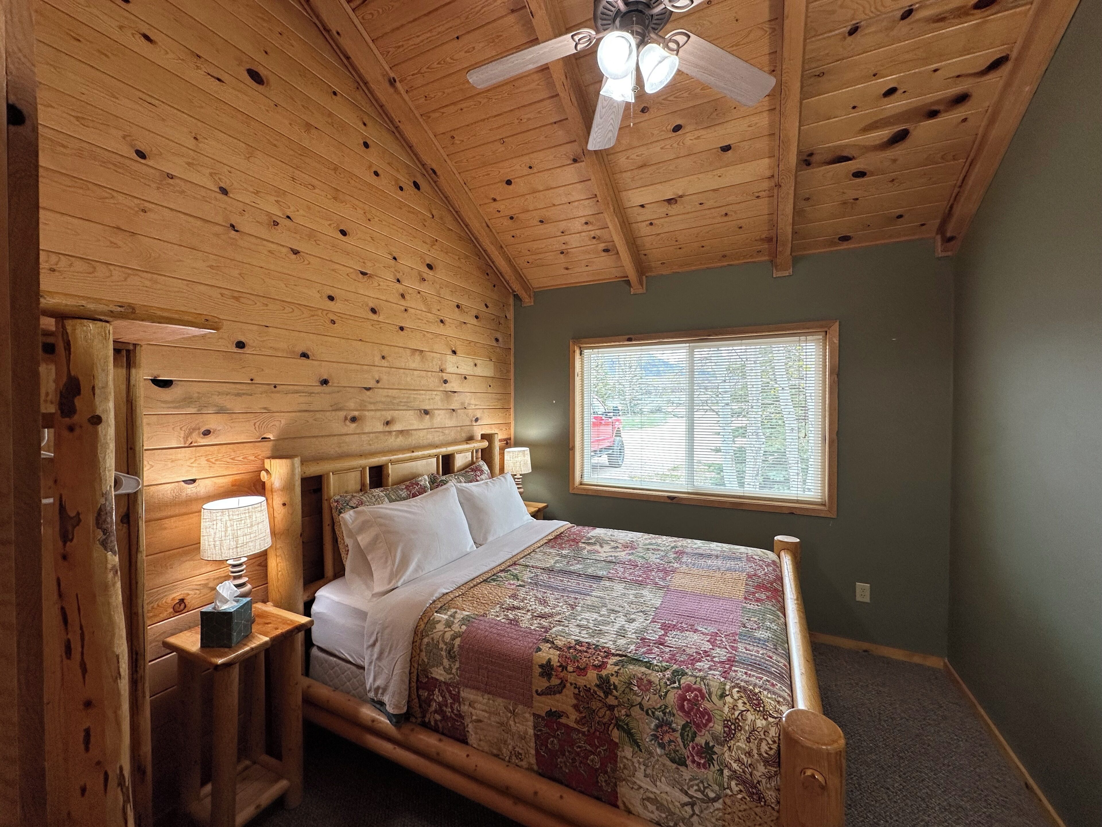 Una habitación de madera con una cama, un ventanal y un ventilador de techo.