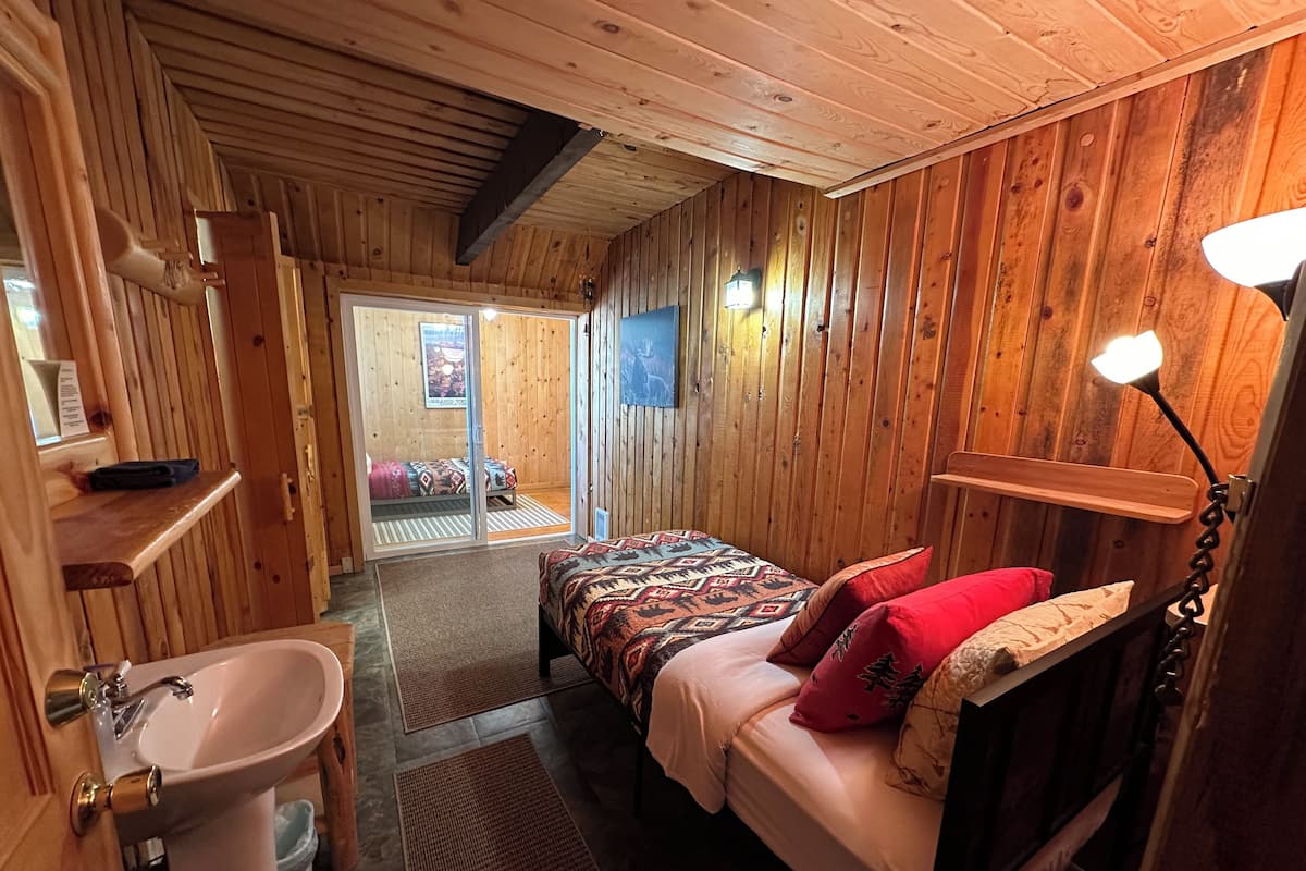 A wooden cabin room with a bed, a sink, and a door leading to a balcony.