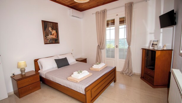 A bedroom with a wooden bed, a nightstand, a dresser, a television, and a painting on the wall. - Giannis House 2022 by Corfu Escapes (Corfu)