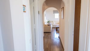 A hallway with wooden flooring, white walls, and an arched doorway leading to a living area with a sofa and a coffee table. - Giannis House 2022 by Corfu Escapes (Corfu)