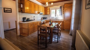 A kitchen with wooden cabinets, a dining table with chairs, a microwave, and a coffee maker. - Giannis House 2022 by Corfu Escapes (Corfu)