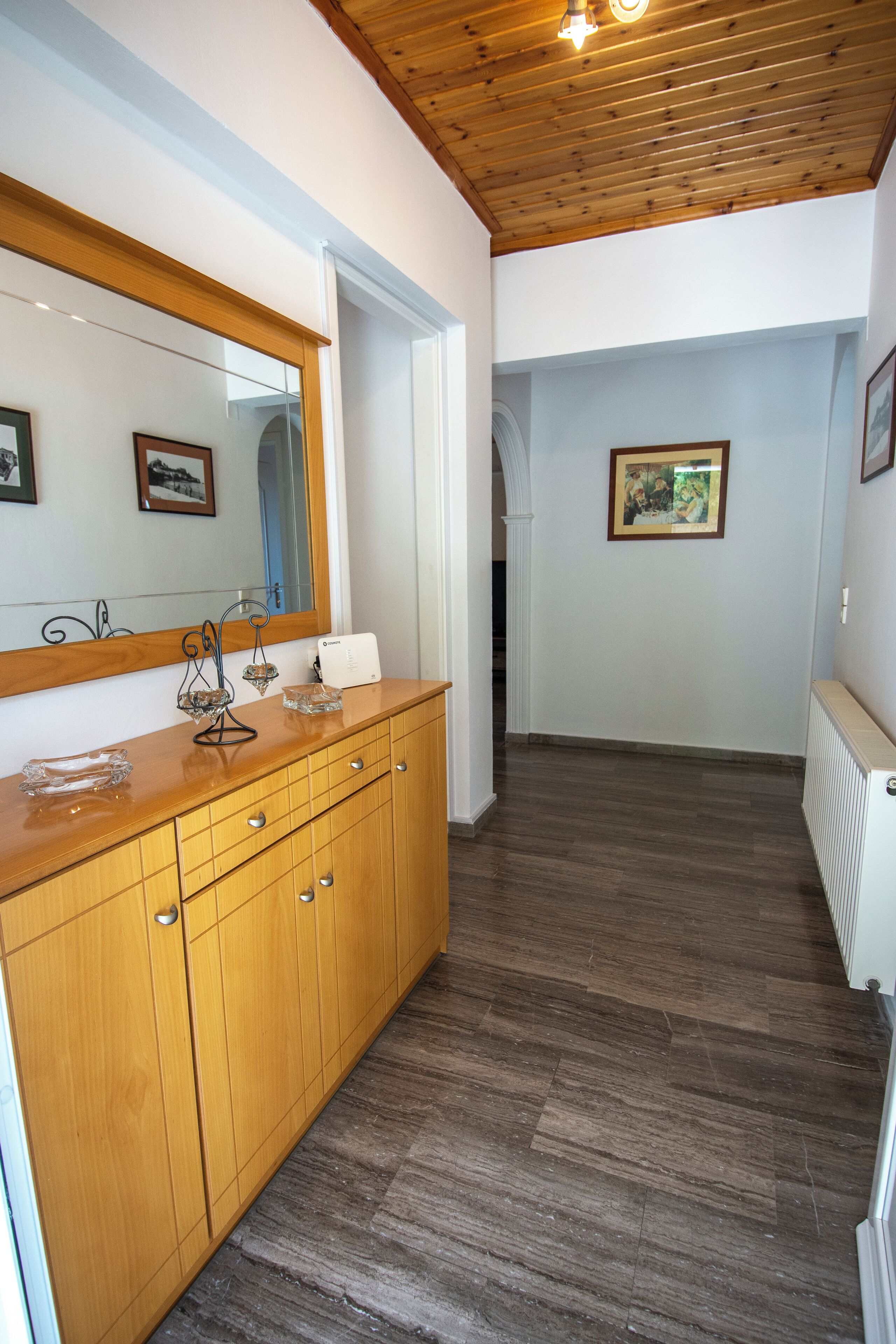 A hallway with wooden flooring, a wooden vanity with a mirror, and framed pictures on the walls.