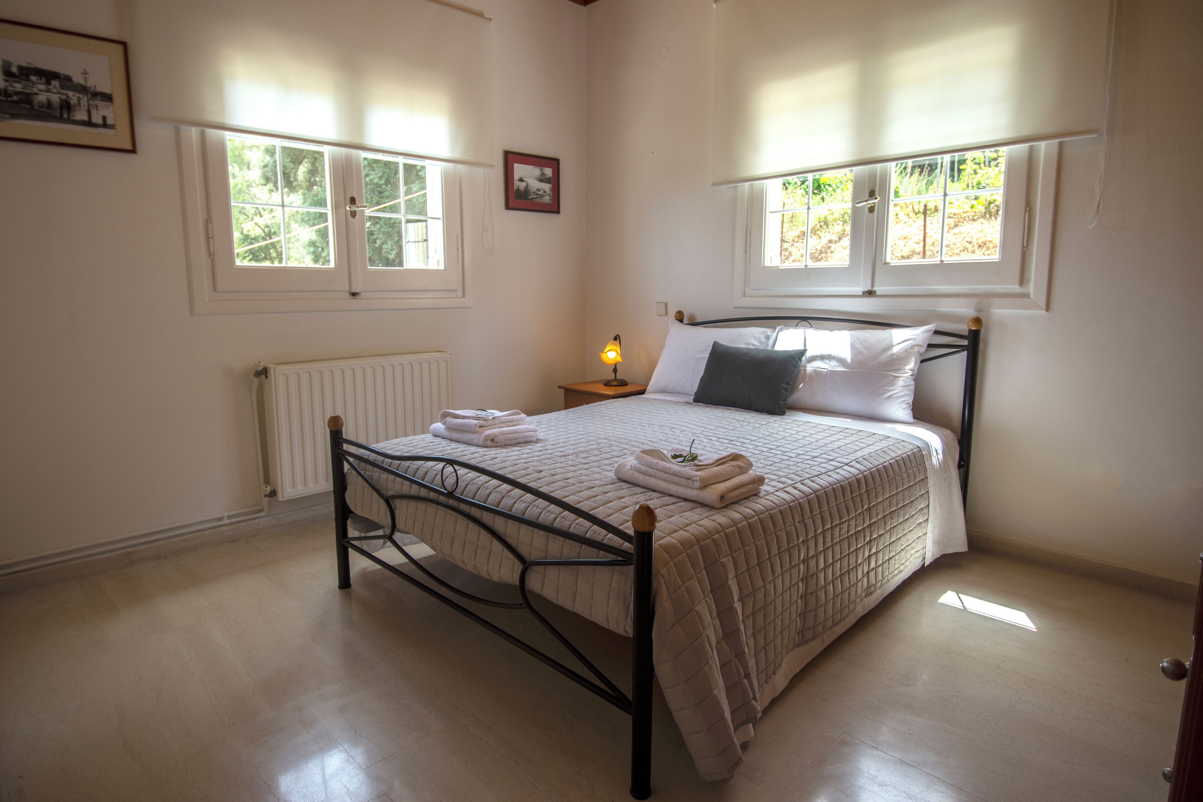Una camera da letto con un letto, un comodino, una lampada e due finestre.