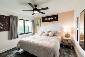 A bedroom with a bed, a ceiling fan, a window with curtains, a wall-mounted artwork, and a nightstand with a lamp. - 400 South (Cocoa Beach)
