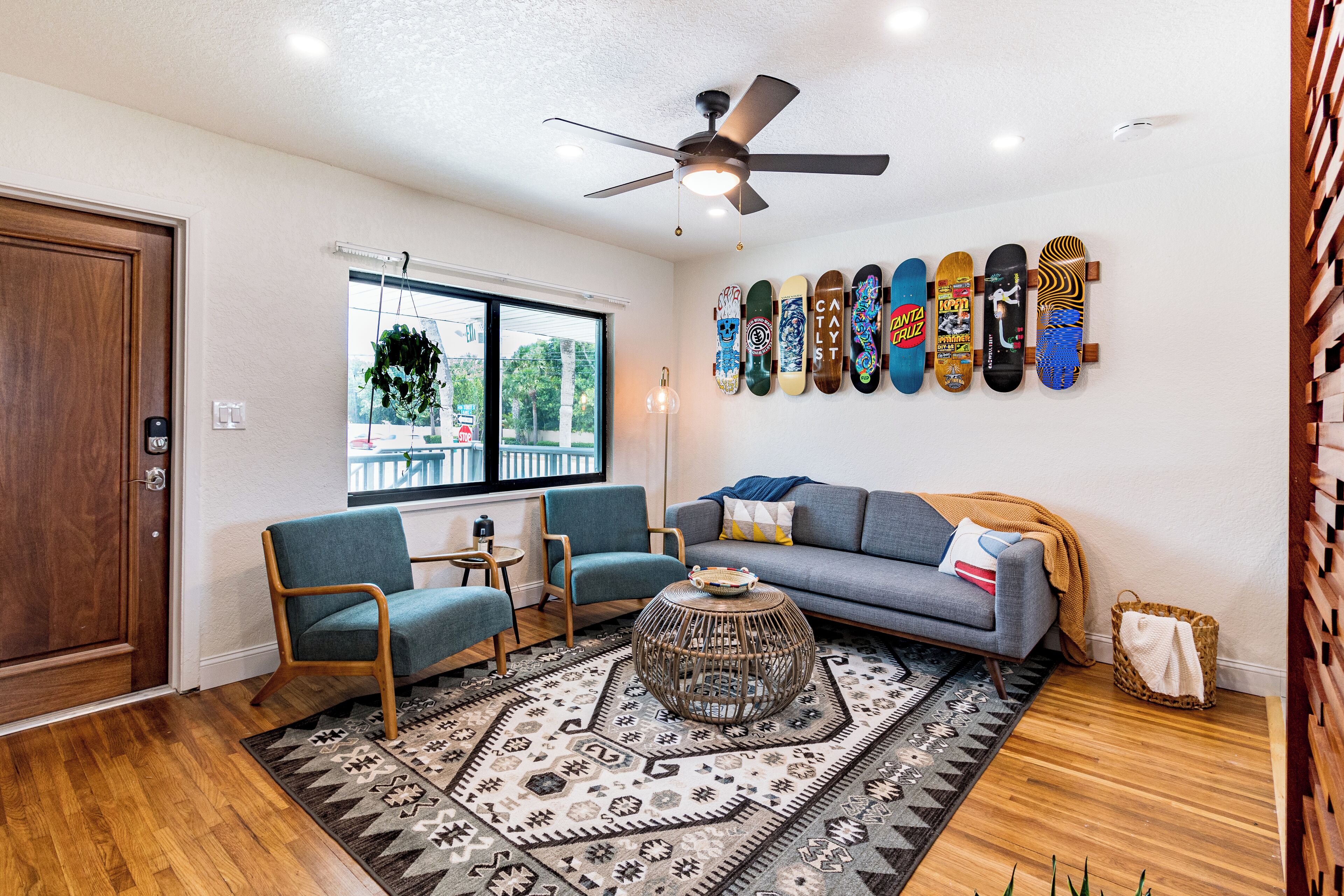 A living room with a sofa, chairs, a coffee table, a ceiling fan, and skateboards on the wall.