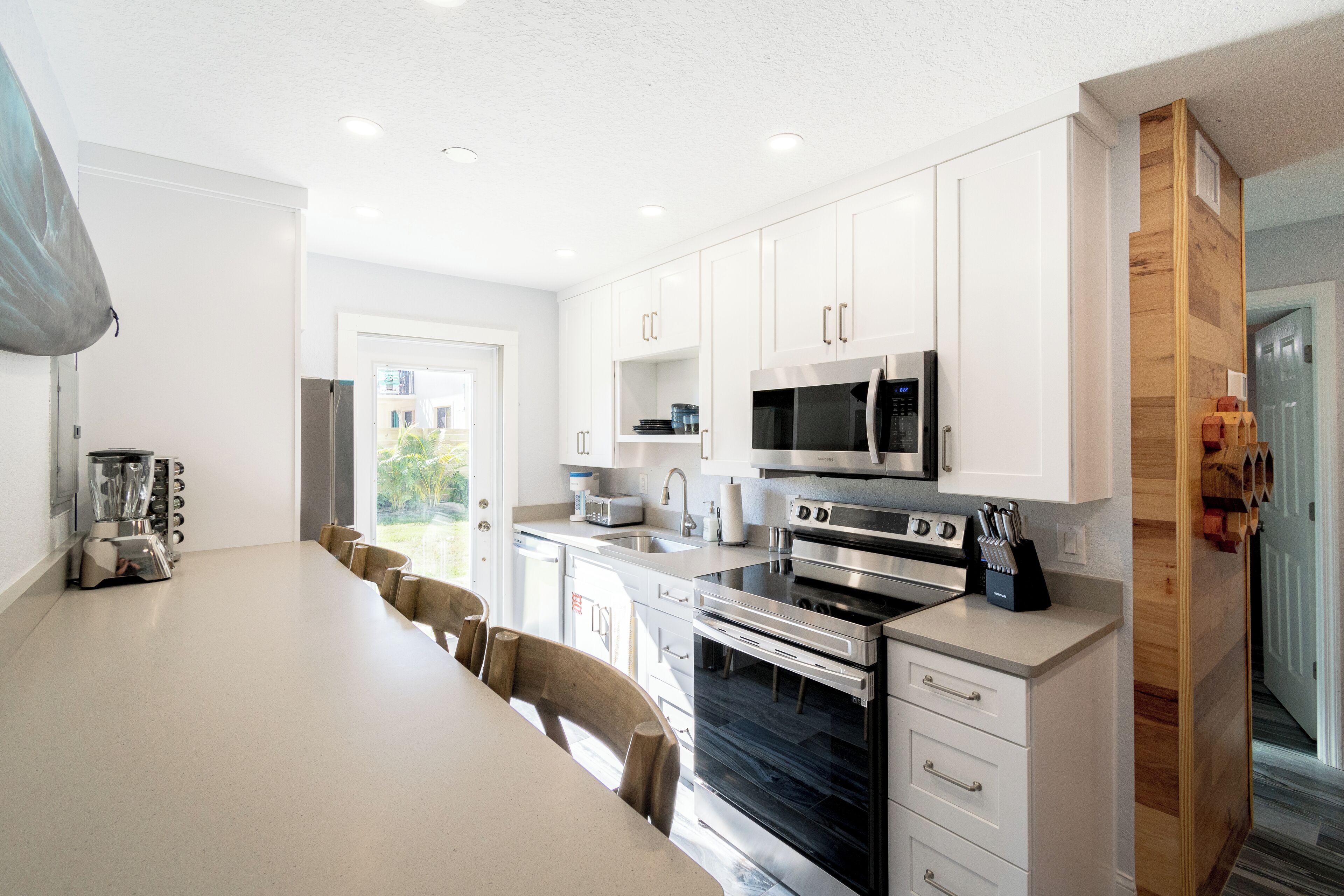 A modern kitchen with white cabinets, stainless steel appliances, and a long dining table.