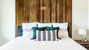 Una cama con cabecera de madera, varios almohadones y una mesita de noche con lámpara.