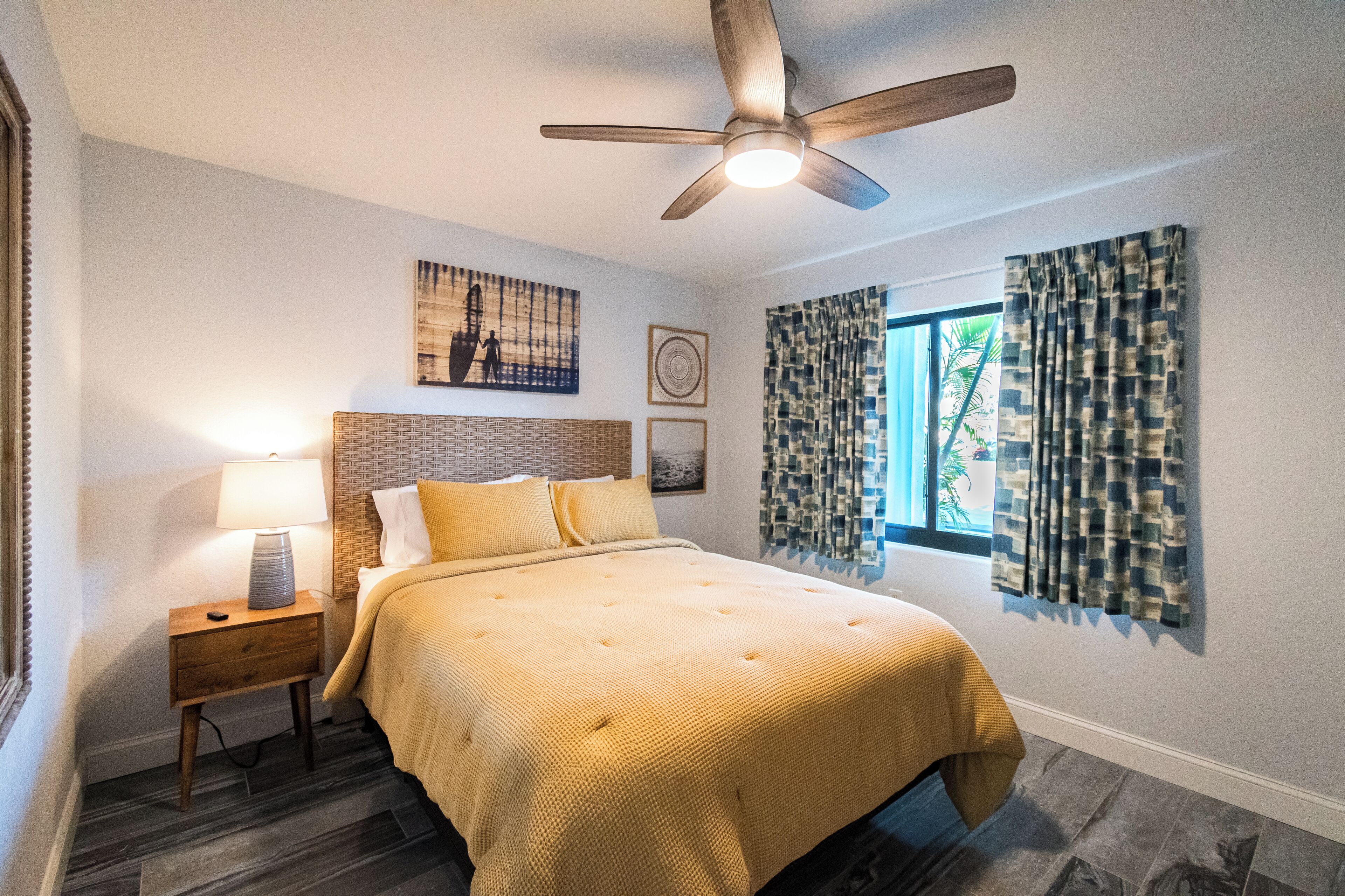 A bedroom with a bed, a nightstand, a ceiling fan, and a window with curtains.