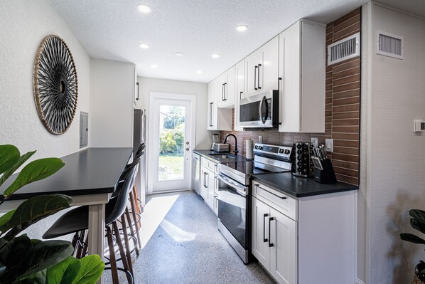 A modern kitchen with white cabinets, stainless steel appliances, and a black countertop. - 400 South (Cocoa Beach)