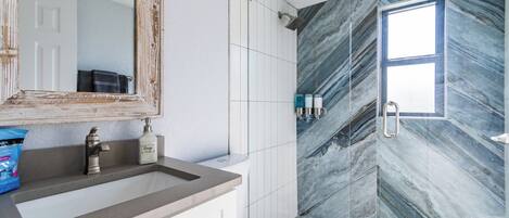 A bathroom with a marble wall, a large mirror, a sink, and a toilet.