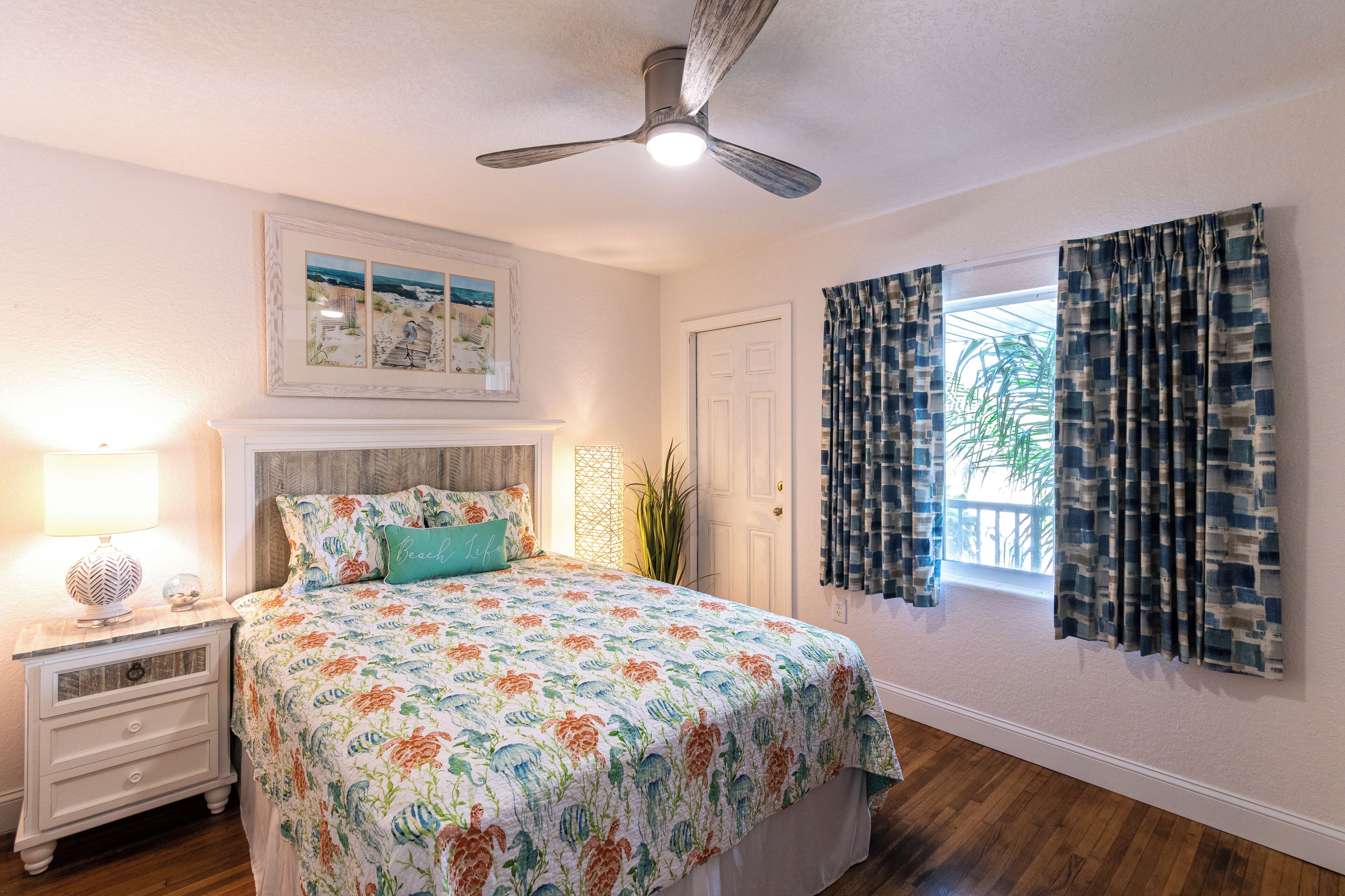 A bedroom with a bed, nightstand, ceiling fan, and a window with curtains.