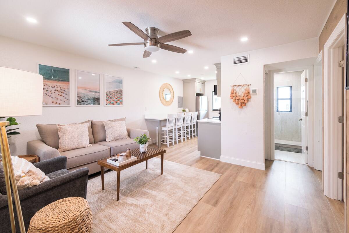 Un salon moderne avec un canapé, une table basse et un ventilateur de plafond. Il y a également un coin cuisine avec un réfrigérateur et une table à manger.