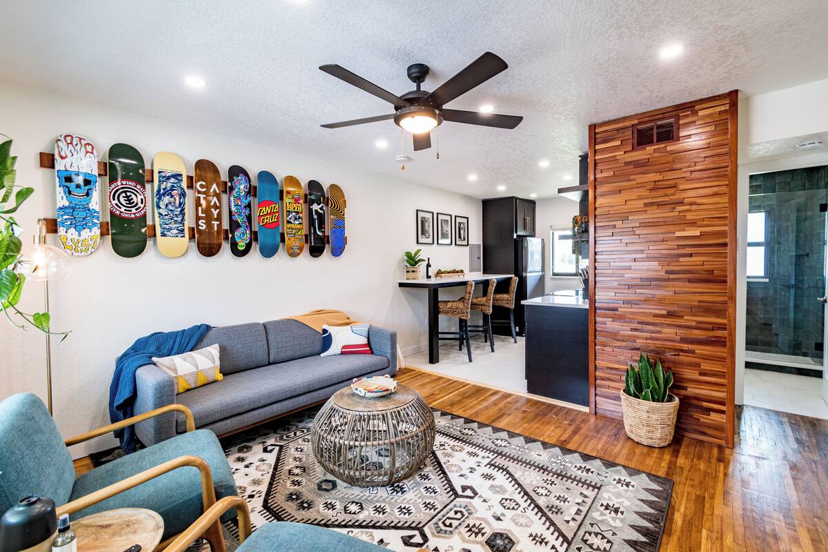 Un salon moderne avec un canapé gris, des fauteuils bleus, une table basse et un mur décoré de planches de skate.