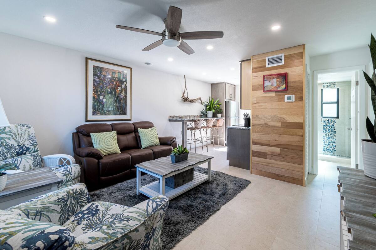 Un salon moderne avec un canapé en cuir marron, un fauteuil à motifs, une table basse et un ventilateur de plafond.