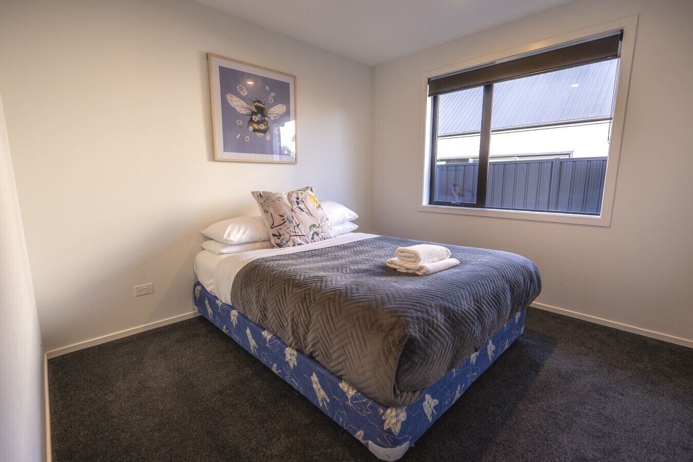A bedroom with a bed, a window, a wall-mounted picture, and a carpeted floor.