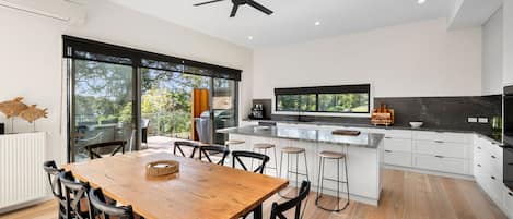 A modern kitchen with a central island, large windows, and a dining area with a wooden table and chairs.