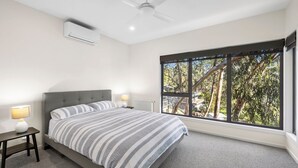 A bedroom with a bed, two bedside tables, a ceiling fan, and a large window with a view of trees. - Coastal View (Lorne)