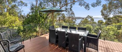 A wooden deck with a glass table and chairs, overlooking a body of water and trees.