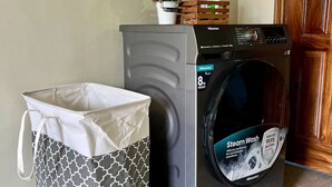 A front-loading Hisense washing machine with a steam wash feature, a patterned laundry basket, and a small potted plant on top. - Theoscozyhaven (Kampala)
