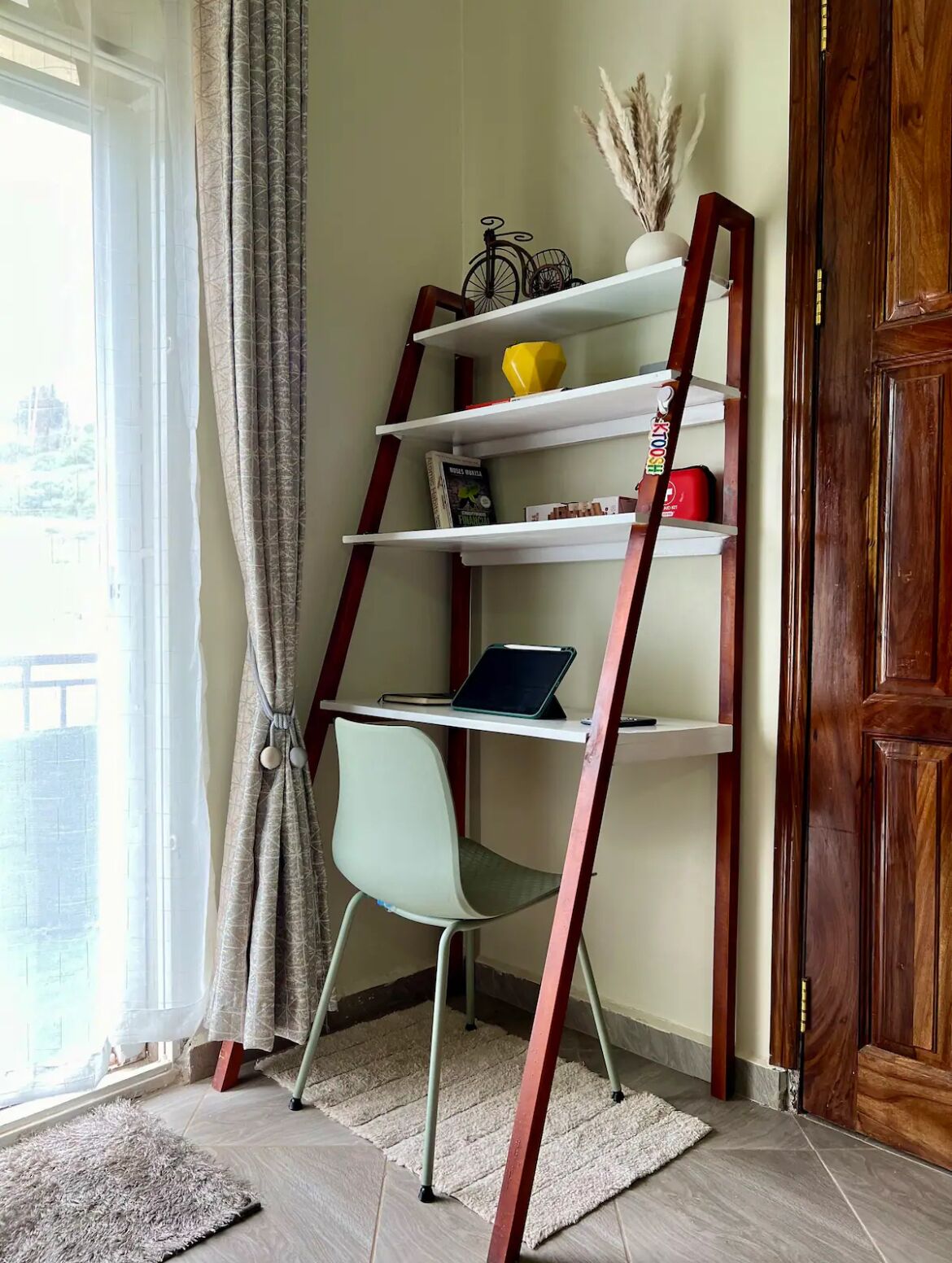 Una habitación en esquina con una estantería de madera escalonada, una silla y una computadora portátil sobre un estante blanco.