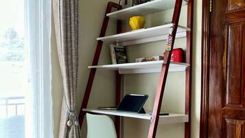 Una habitación en esquina con una estantería de madera escalonada, una silla y una computadora portátil sobre un estante blanco.
