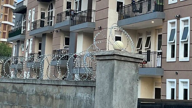 A multi-story residential building with balconies, a stone wall, and barbed wire. - Theoscozyhaven (Kampala)