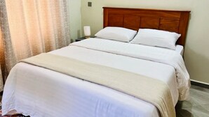 A neatly made bed with a wooden headboard, white bedding, and a bedside lamp. - Theoscozyhaven (Kampala)