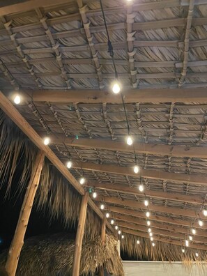 Estructura con techo de paja, vigas de madera y luces colgantes.