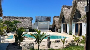 Un resort con edificios de techo de paja, piscina y cielo azul despejado.