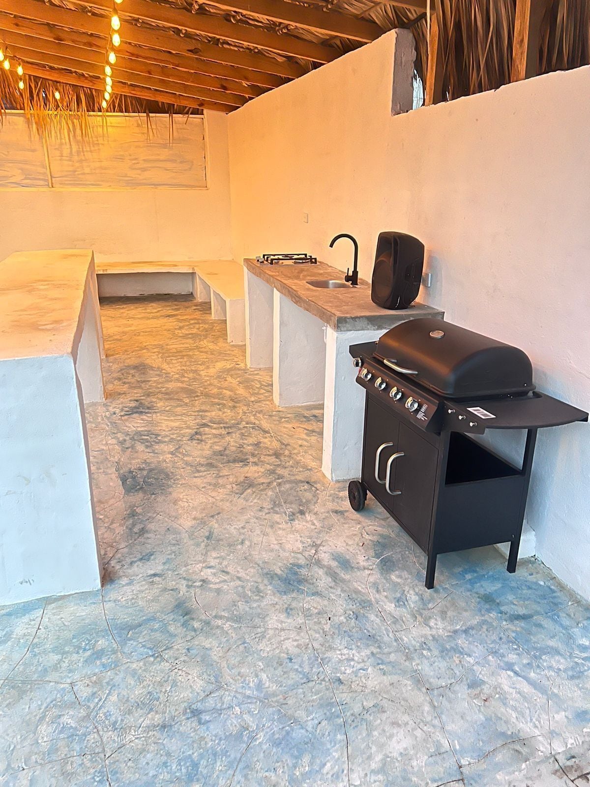 An outdoor kitchen area with a grill, sink, and bar stools.