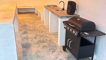 Un espace cuisine extérieur comprenant un barbecue, un évier et des tabourets de bar.