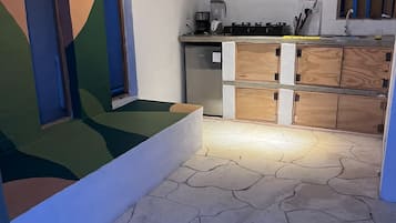 Cocina compacta con refrigerador, estufa y repisas con utensilios de cocina.