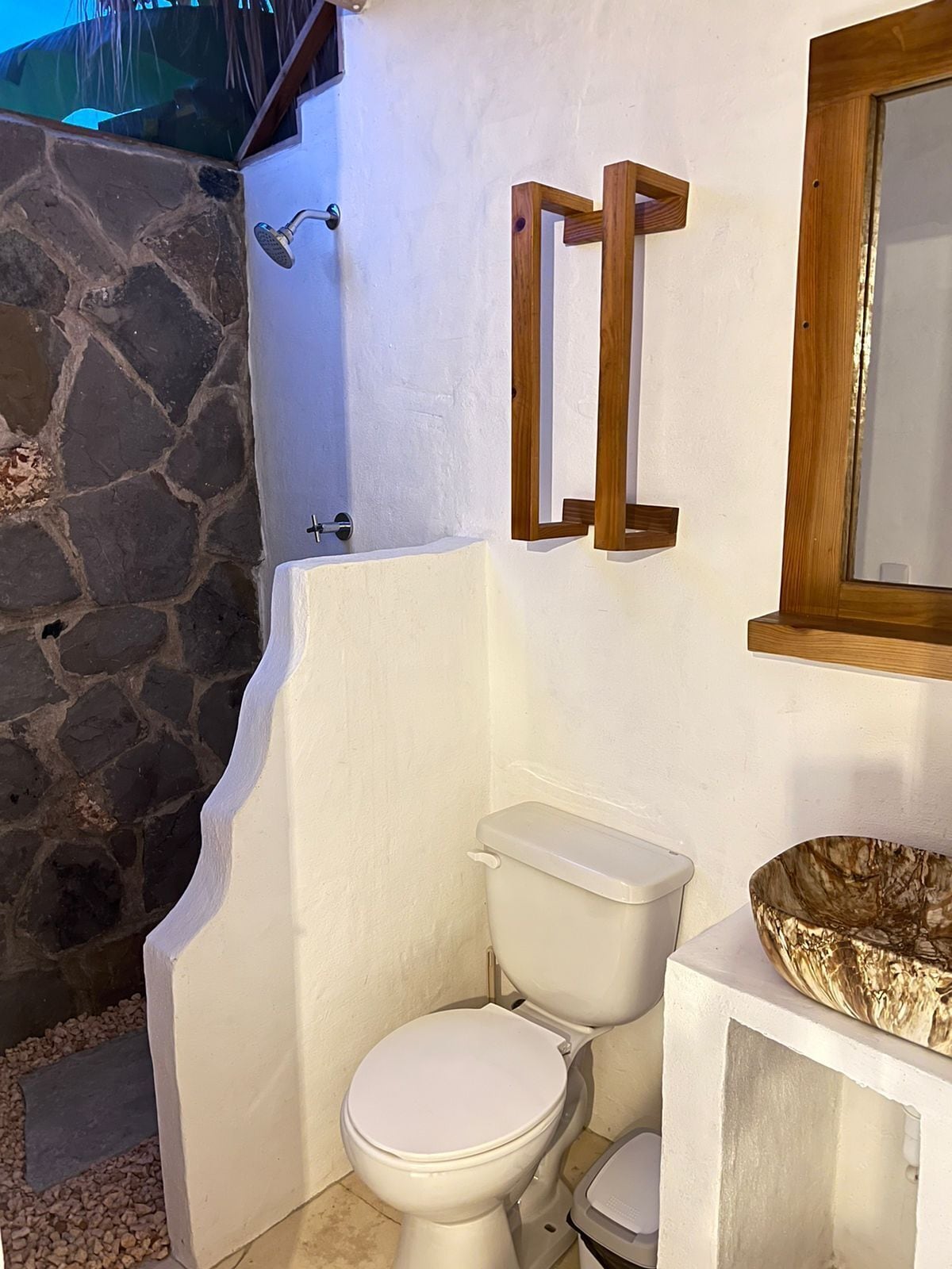 Een badkamer met een wit toilet, een stenen muur en een spiegel met houten lijst.