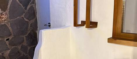 A bathroom with a white toilet, a stone wall, and a wooden-framed mirror.