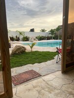 Vista de una piscina con un patio de piedra, una pequeña palmera y una silla roja.