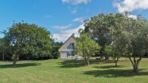 Une maison avec un toit en pente, entourée d’une pelouse verdoyante et d’arbres.