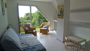 Une chambre à coucher avec un lit, une petite table et une chaise. Il y a une fenêtre donnant sur un paysage verdoyant.