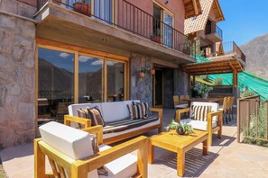 A patio with wooden furniture, a stone wall, and a balcony with potted plants. - Catahuasi by Wynwood House (Huayllabamba)