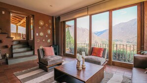 A spacious living room with a large window overlooking mountains, a staircase, and a cozy seating area. - Catahuasi by Wynwood House (Huayllabamba)