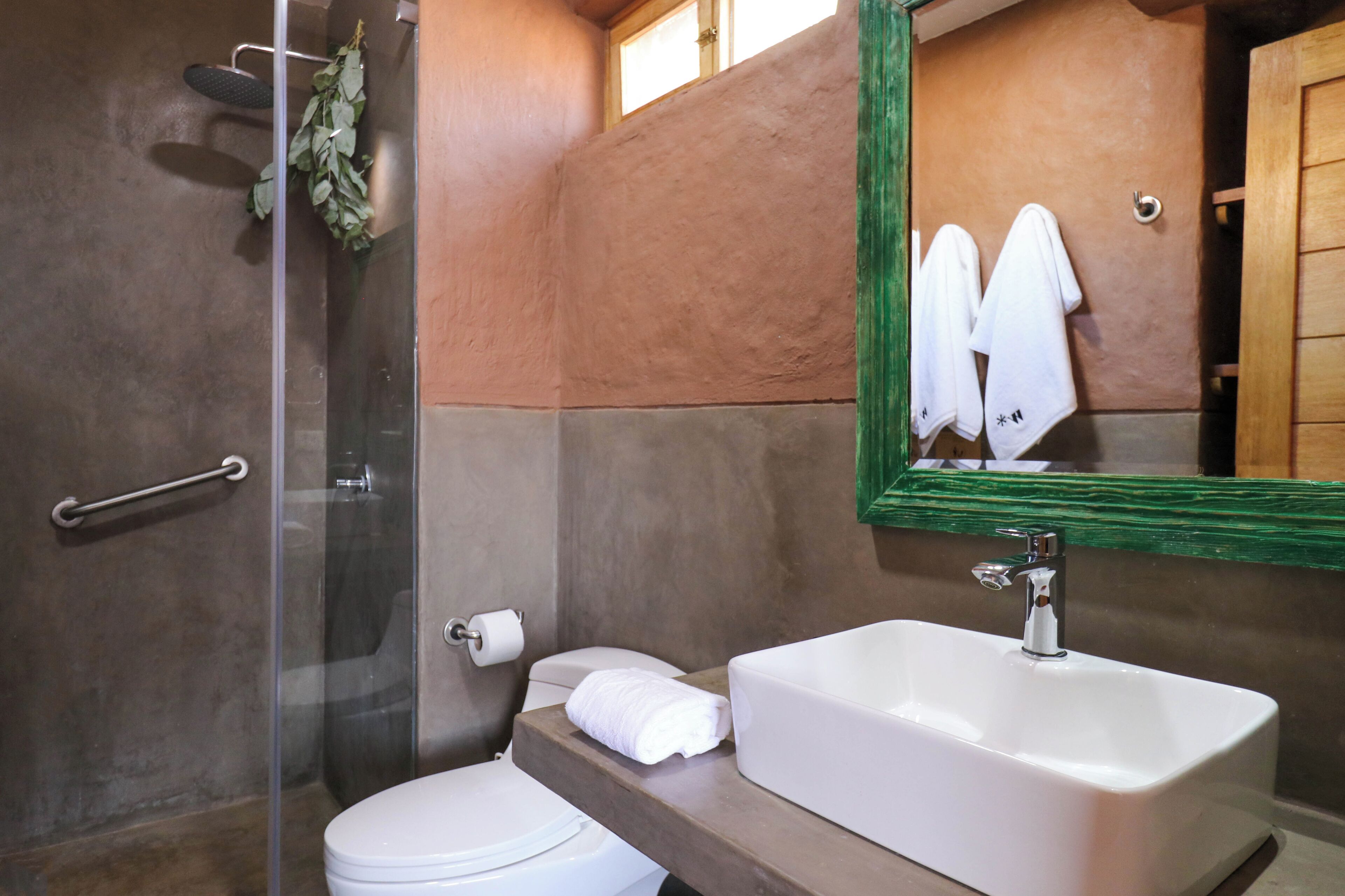 A bathroom with a glass shower enclosure, a white sink, and a mirror with a green frame.