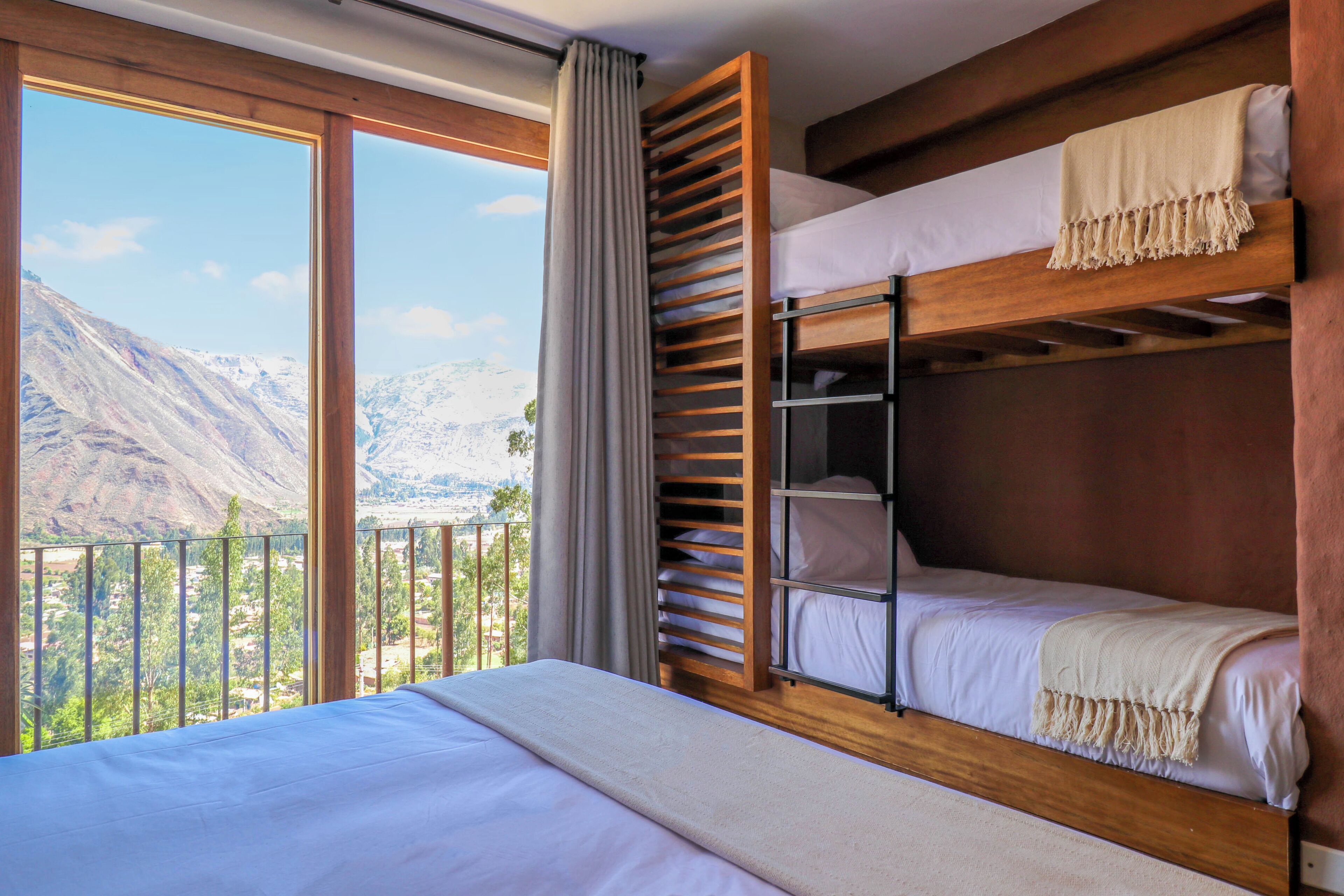 A room with a bunk bed, a large window with a view of mountains, and a balcony.