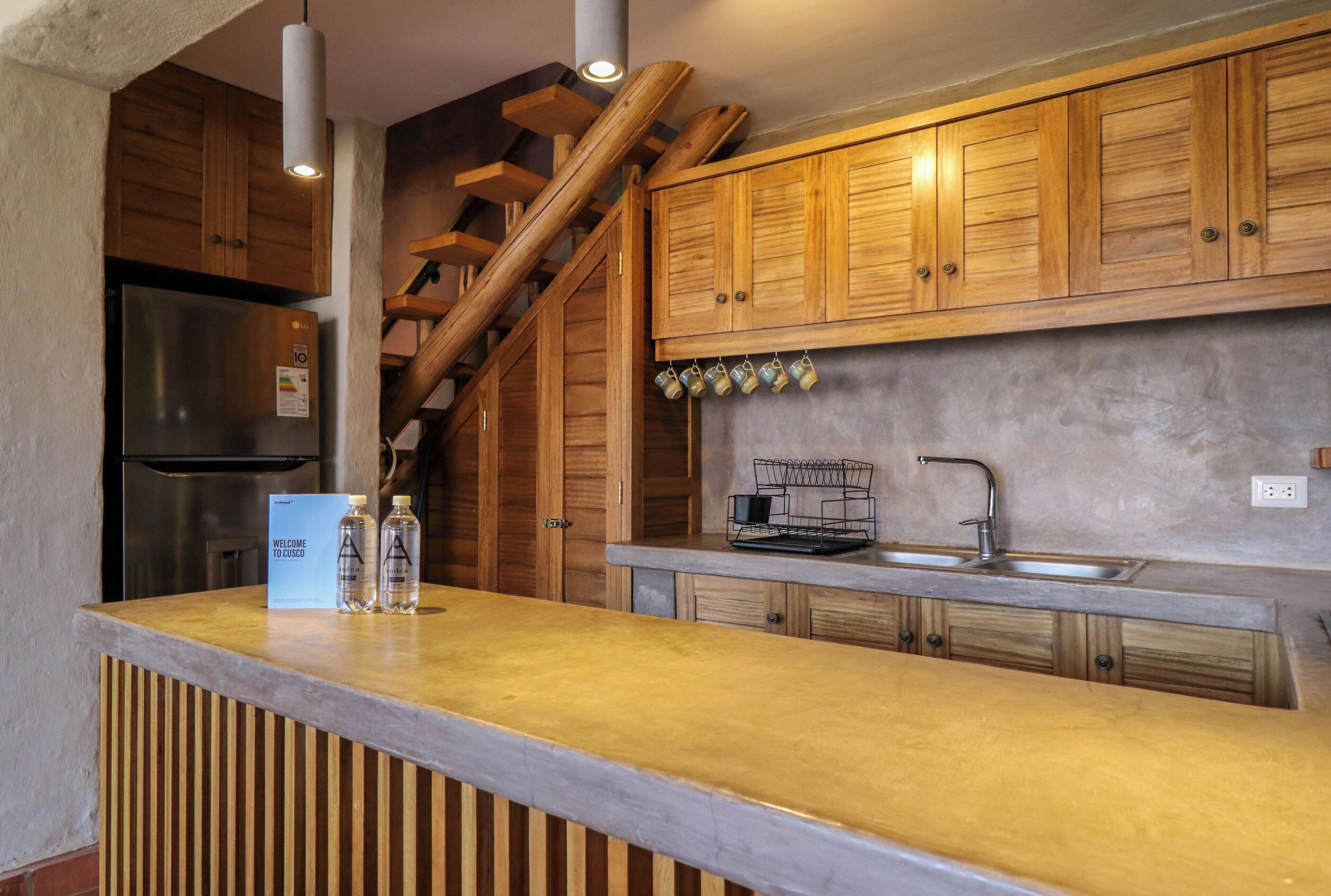 A kitchen with wooden cabinets, a stainless steel refrigerator, a sink, and a bar area with a welcome sign.