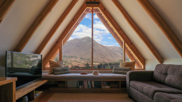 A cozy attic room with a large window offering a mountain view, a comfortable sofa, a television, and a bookshelf. - Catahuasi by Wynwood House (Huayllabamba)